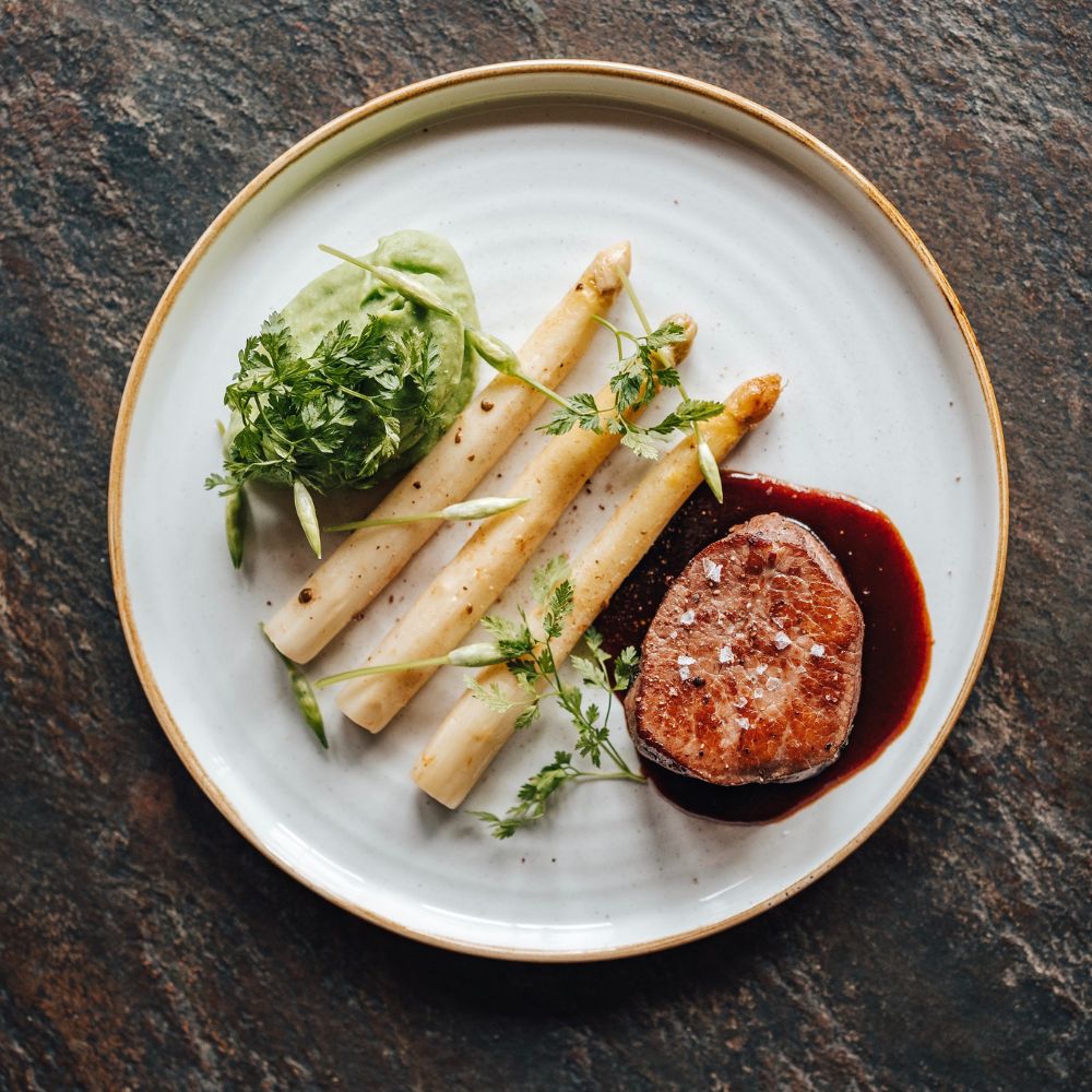 Telecí steak s bílým chřestem, máslem, fermentovaným pepřem a s bramborovým pyré s medvědím česnekem podle šéfkuchaře Miloše Nováka